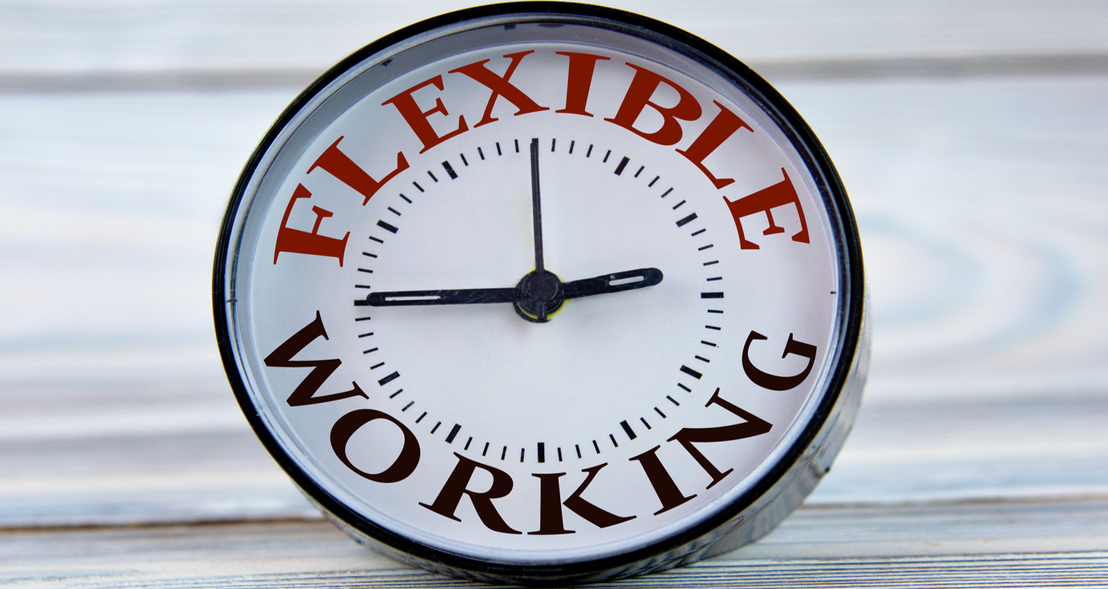 Alarm clock with words FLEXIBLE WORK on light wooden background close-up. Business concept